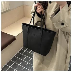 Detail of black pebbled leather tote bag with brand embossing worn with a beige trench coat