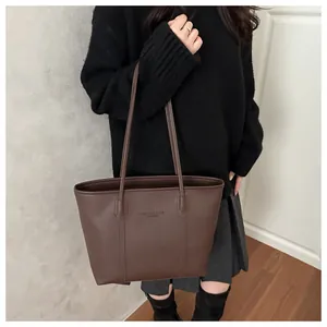 Detail of minimalist dark brown tote bag showing pebbled leather texture and embossed logo