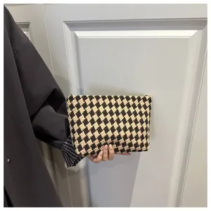Detail of a brown and beige checkered knit clutch bag held against a white door