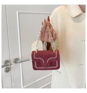 Close-up of wine red suede mini crossbody bag featuring white stitching and gold chain