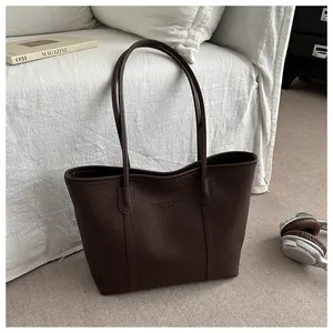 Detail of dark brown lychee leather tote bag with embossed fashion text and long straps