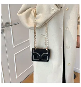 Close-up of black suede mini crossbody bag with white V-stitch detailing and gold chain strap