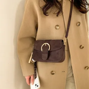 Detail of vintage brown suede crossbody bag with gold buckle and creative baseball charm