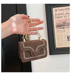 Detail of brown suede handbag featuring white wavy embroidery and gold chain handle