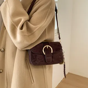 Detail of dark brown suede crossbody bag with gold horseshoe buckle on model coat