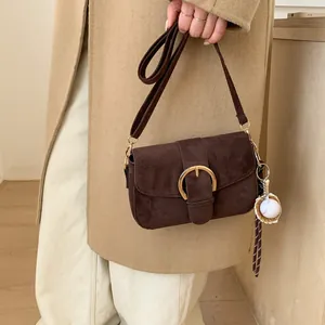 Detail of vintage brown suede crossbody bag with gold horseshoe buckle and baseball charm