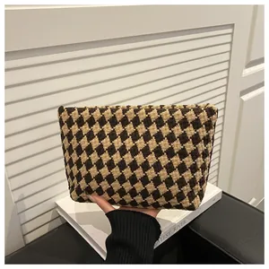 Close-up of a brown houndstooth tweed clutch bag held over white decorative books