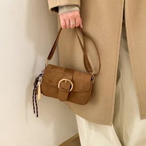 Detail of caramel brown matte handbag with a large gold ring buckle and woven tassel