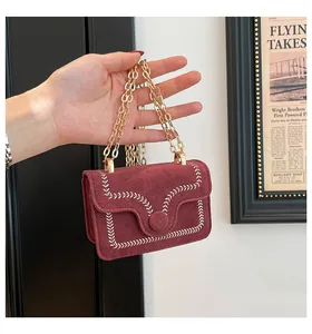 Detail of burgundy suede mini bag featuring white embroidery stitching and gold chain