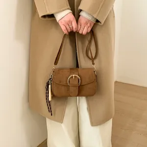 Detail of a brown suede crossbody bag with large gold buckle and woven tassel on a model