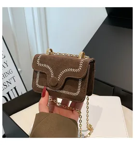 Detailed close-up of brown suede bag with white stitching and golden chain strap