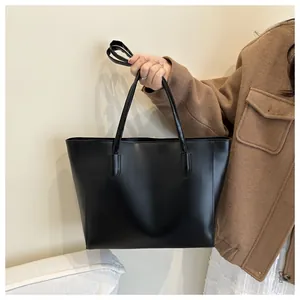 Close-up of a matte black tote bag with slender straps held by a model in a beige coat