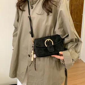 Detail of black suede shoulder bag with gold horseshoe buckle and baseball charm