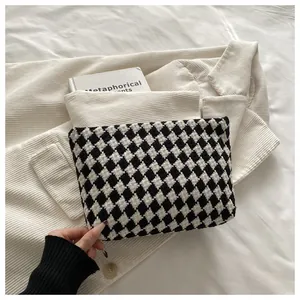 Detail of black and white checkered knit clutch bag on a textured fabric background
