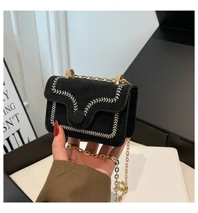 Detail of a mini black suede crossbody bag with elegant white leaf embroidery and gold chain
