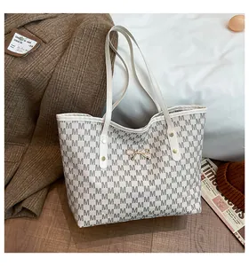 Détail du sac cabas crème avec motif de lettres M et breloque noeud doré élégante