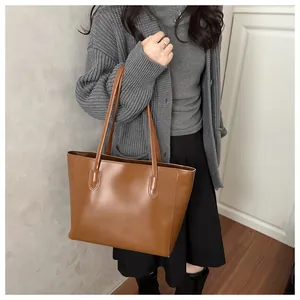 Brown large-capacity tote bag with long handles shown on model in a cozy home setting