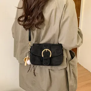 Detail of black suede flap crossbody bag featuring large gold buckle and sports charm