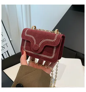 Detail of wine red suede bag featuring contrast white stitching and gold chain strap