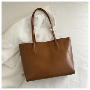 Detail of brown leather tote bag with thin straps on white corduroy background