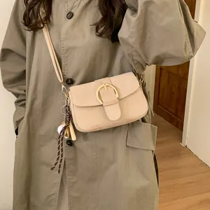 Detail of a beige flap bag featuring a large gold buckle and a decorative baseball charm