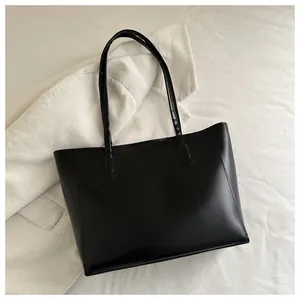Flat lay of minimalist black leather tote bag with long straps on white fabric background