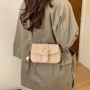 Detail of beige suede crossbody bag with gold buckle and baseball charm on a model