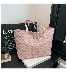 Détail d'un sac cabas rose avec motif à lettres M et nœud doré posé sur des livres