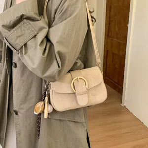Detail of beige faux suede crossbody bag with gold buckle and sports charms