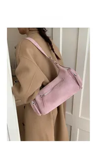 Close-up of pink suede cylinder bag with silver zipper detail on model in camel coat