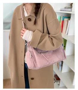 Pink faux suede crossbody bag with zipper details worn over a stylish long camel coat