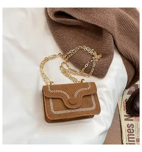 Close-up of brown suede bag with elegant white embroidery and a gold chain strap