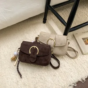 Detail of retro suede crossbody bag with gold buckle and baseball charm on beige carpet