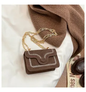 Detail of brown suede crossbody bag featuring white wavy embroidery and gold chain strap