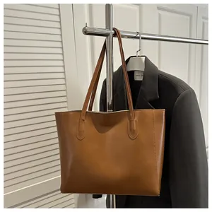 Detailed view of caramel PU leather tote bag with sturdy stitching on a metal hanger