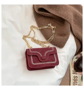 Detailed macro view of burgundy suede crossbody bag with elegant white embroidered trim
