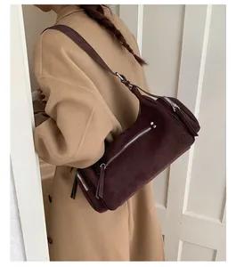 Detailed macro view of dark brown suede cylinder bag with silver metal zippers and long pulls