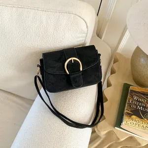 Detail of black suede flap bag featuring a gold D-ring buckle on a cream sofa