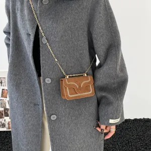 Brown suede crossbody bag with wavy stitching and chain strap shown on model coat