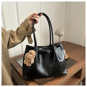 Detail of black faux leather tote bag featuring belt buckle strap and plush dog pendant