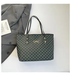 Vue à plat du sac cabas avec motif M, détail de nœud doré et fond de magazine