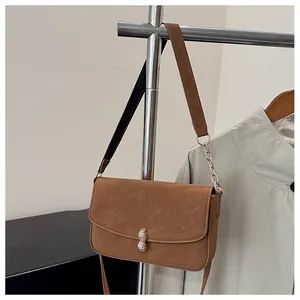 Detail view of brown crossbody bag with unique golden peanut-shaped buckle and chain strap