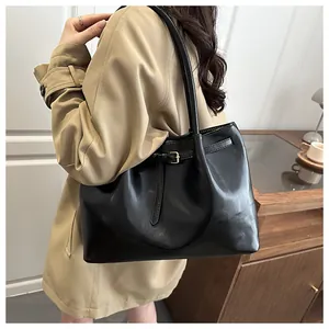 Close-up of black leather tote bag with metallic buckle detail on soft trench coat