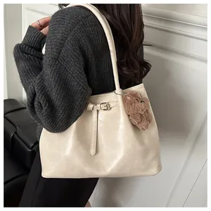Detail view of beige faux leather tote bag with decorative buckle strap and plush bear charm