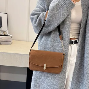 Brown crossbody bag with peanut-shaped gold clasp and chain strap on a model