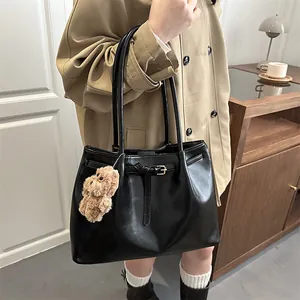 Black leather tote bag with decorative buckle and bear charm on model in trench coat