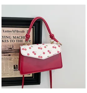 Detail of red cherry print and glossy finish on a stylish small square women's handbag