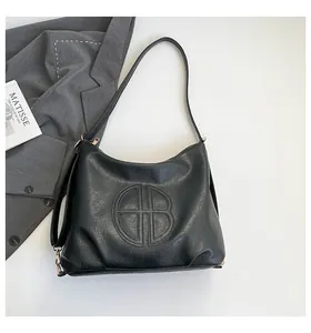 Detail of black pebbled leather tote bag with embossed round logo and gold hardware accents