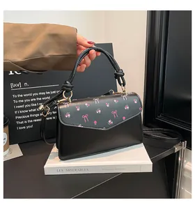 Close-up of black leather crossbody bag with pink floral flap and gold hardware