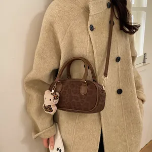 Brown leopard print Boston bag with plush kitty charm worn over a beige coat